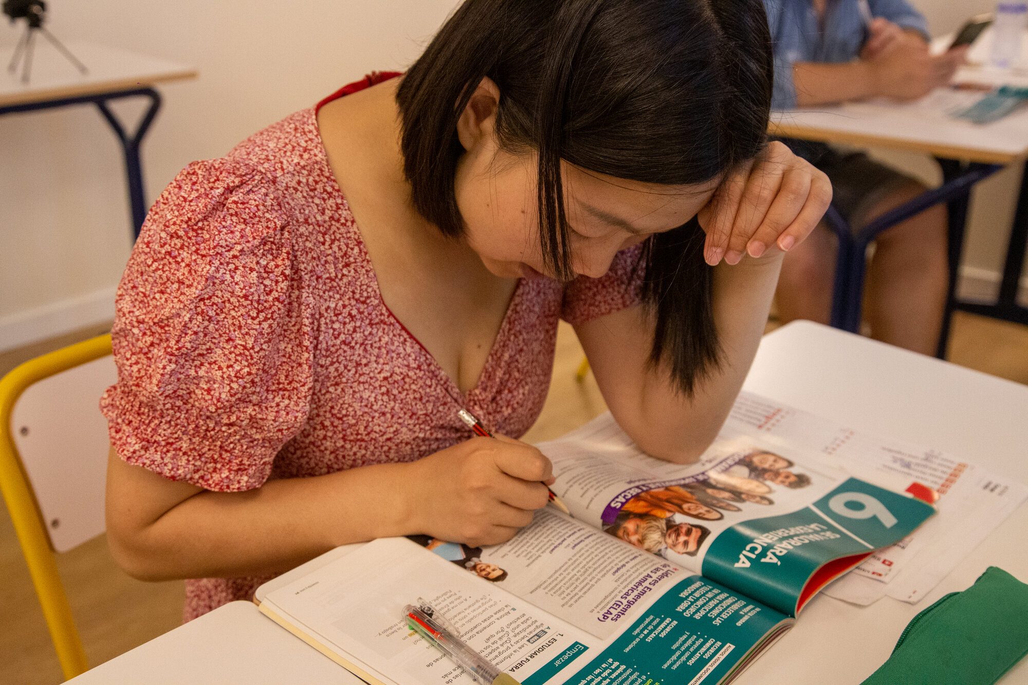 Young woman in a floral dress leaning over and writing with focus